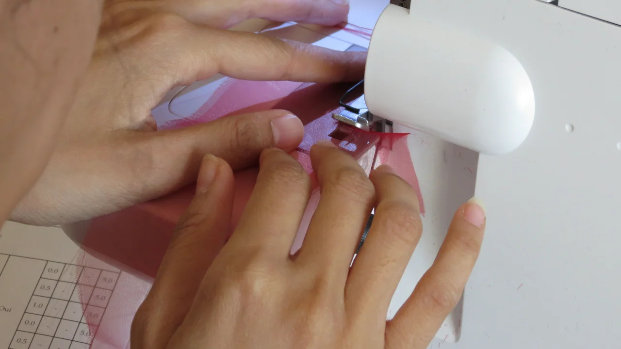 Overlok makinesinde pembe kumaşın kenarını temizleyen eller